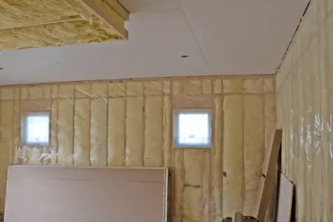 Isolation plafond garage en cours, murs recouverts de laine de verre et pare-vapeur. Deux petites fenêtres laissent passer la lumière.