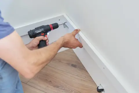 Un bricoleur utilise une visseuse pour fixer du placo sous pente, créant ainsi un espace de rangement fonctionnel.