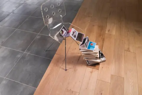 Une jonction carrelage parquet sans barre de seuil, avec une chaise transparente et des livres.