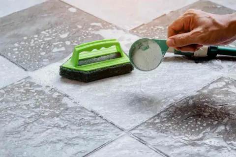 Nettoyer carrelage mural encrassé avec une éponge verte et une poudre nettoyante.