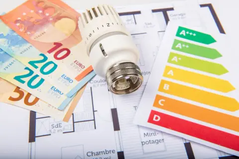 Billets en euros, thermostat et étiquette énergie sur un plan de maison. Un audit énergétique de maison pour optimiser les dépenses.