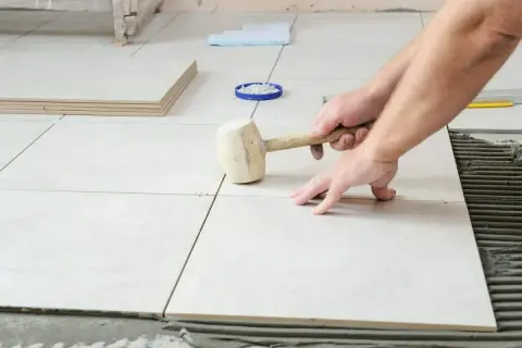 Pose de carrelage : un artisan utilise un maillet pour ajuster une nouvelle dalle sur le mortier.