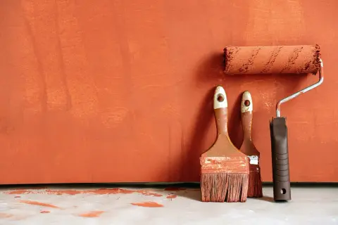 Pinceaux et rouleau de peinture orange sur fond texturé. Idéal pour savoir comment rattraper une peinture mal faite.