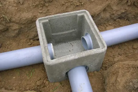 Pose regard béton pour l'eau pluviale, avec des tuyaux gris en PVC installés dans la terre.