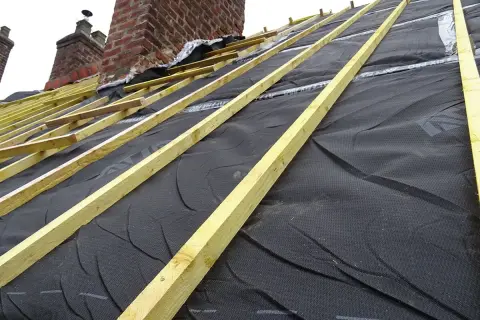 Charpente en cours d'installation, avec la membrane d'étanchéité noire prête pour l'isolation toiture. Les chevrons en bois sont posés.
