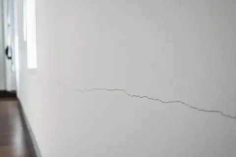 Un fin mur qui s'effrite, marqué par une longue fissure sinueuse, témoigne du passage du temps dans un couloir lumineux.