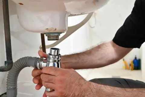 Main tenant en main le siphon, il procède au démontage du siphon de la baignoire pour une réparation.