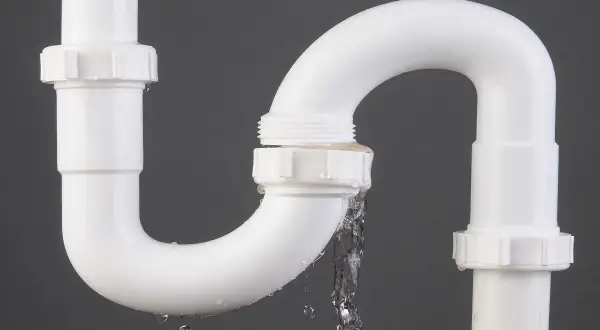 Tuyau de PVC blanc avec une fuite d'eau. Le temps de séchage de la colle PVC est crucial pour éviter ce genre de problème.