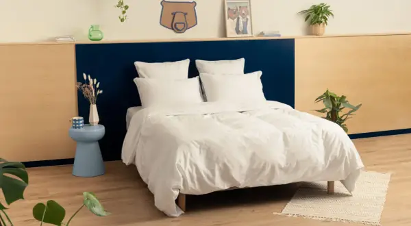 Une chambre adulte avec une tête de lit bicolore, bleu marine et bois clair. Le lit est fait de draps blancs immaculés.