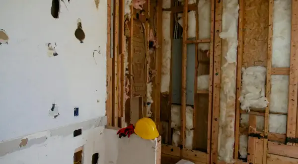 Chantier en cours, murs ouverts révélant l'isolant. Attention, la laine de bois peut présenter un danger si mal manipulée. Casque et gants de protection à proximité.