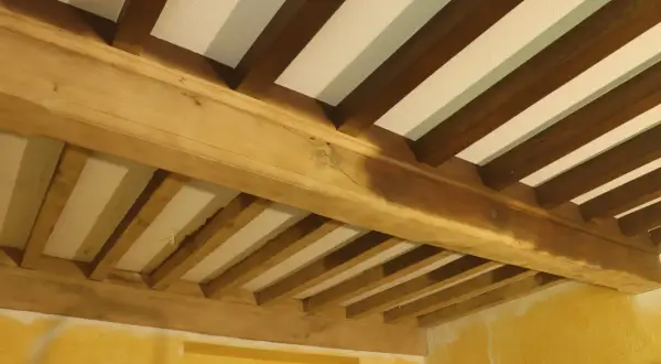Poutres en bois brutes, prêtes pour le sablage, soutenant un plafond blanc. La texture naturelle du bois est visible.