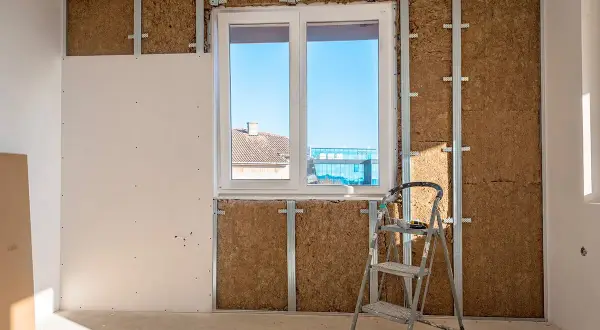 Travaux d'isolation intérieure : murs en cours de pose, avec laine de bois visible derrière une ossature métallique et une plaque de plâtre. Une échelle est présente.