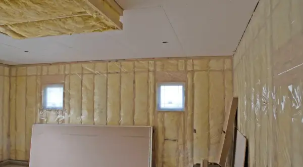 Isolation plafond garage en cours, murs recouverts de laine de verre et pare-vapeur. Deux petites fenêtres laissent passer la lumière.