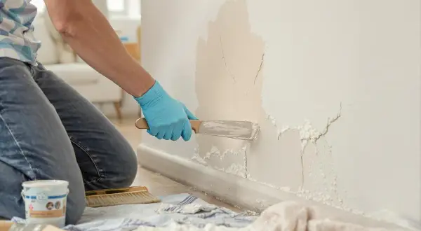 Un artisan répare une fissure sur un mur intérieur avec une spatule.