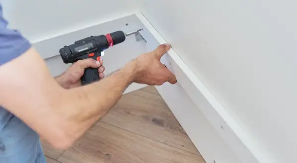 Un bricoleur utilise une visseuse pour fixer du placo sous pente, créant ainsi un espace de rangement fonctionnel.