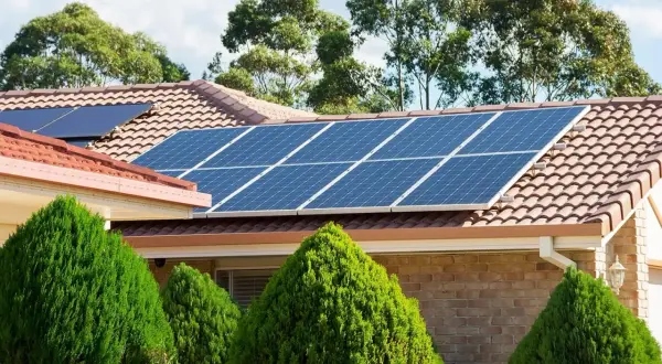 Panneaux solaires thermiques bleus brillants sur un toit de tuiles, entourés de verdure luxuriante.
