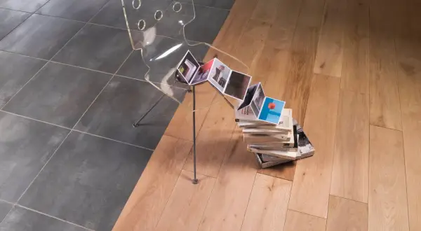 Une jonction carrelage parquet sans barre de seuil, avec une chaise transparente et des livres.
