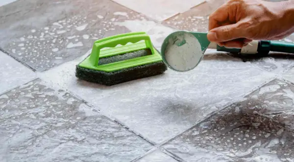 Nettoyer carrelage mural encrassé avec une éponge verte et une poudre nettoyante.
