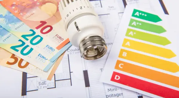 Billets en euros, thermostat et étiquette énergie sur un plan de maison. Un audit énergétique de maison pour optimiser les dépenses.