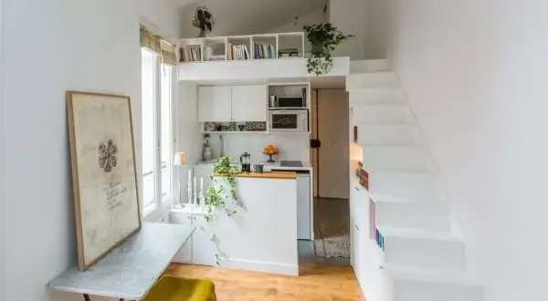 Un petit appartement optimisé pour le rangement, avec une cuisine, un coin repas et des escaliers menant à une mezzanine.