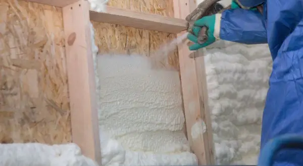 Application de polyuréthane projeté pour isoler une structure en bois. La mousse blanche s'étend, créant une barrière isolante.
