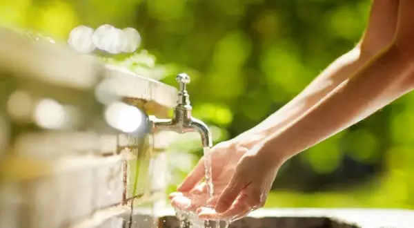 Mains sous un robinet extérieur. La hauteur du robinet extérieur est idéale pour se laver les mains dans ce cadre verdoyant.