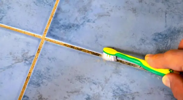 Main tenant, une brosse à dents verte et jaune est utilisée pour nettoyer joint salle de bain.