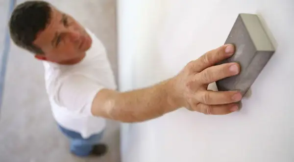 Un homme ponce un mur blanc avec une cale à poncer, préparant la surface avant de peindre.