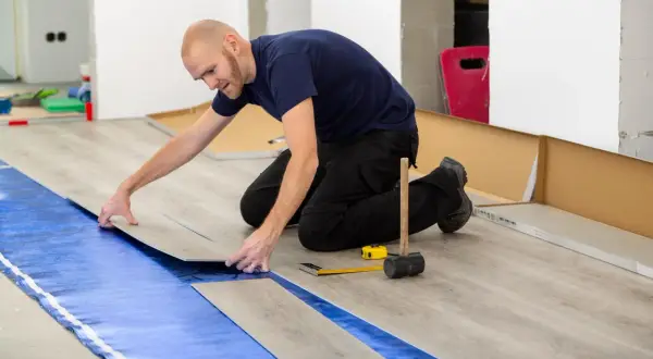 Pose d'un revêtement de sol stratifié sur une isolation sous carrelage. L'homme pose une lame de parquet.