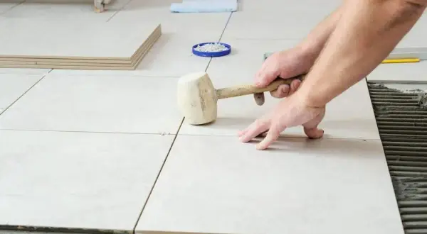 Pose de carrelage : un artisan utilise un maillet pour ajuster une nouvelle dalle sur le mortier.