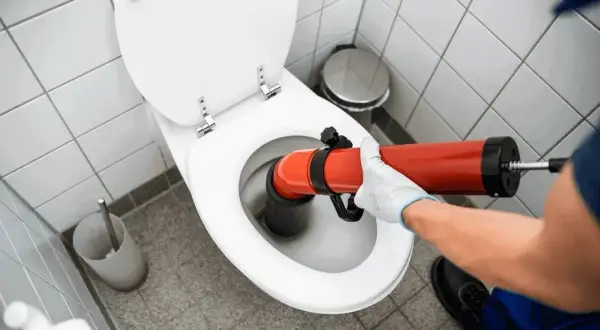 Main tenant utilise un déboucheur pour déboucher WC.