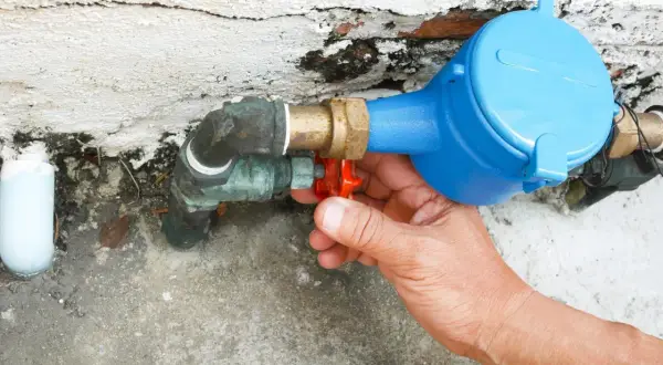 Main tenant intervient pour réparer une fuite d'eau sur un raccord de compteur.