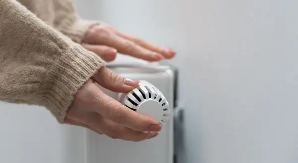 Mains mains sur un radiateur, ajustant le thermostat pour contrôler le prix du chauffage au gaz.