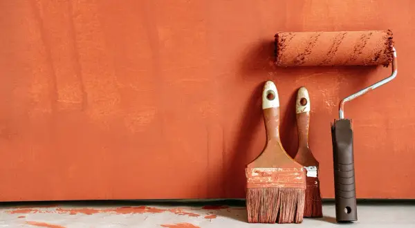 Pinceaux et rouleau de peinture orange sur fond texturé. Idéal pour savoir comment rattraper une peinture mal faite.