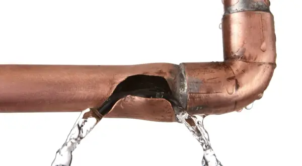Une fuite sur un tuyau en cuivre provoque un jet d'eau. L'eau s'échappe d'une fissure béante dans le métal.