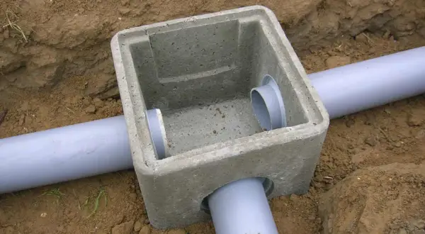 Pose regard béton pour l'eau pluviale, avec des tuyaux gris en PVC installés dans la terre.