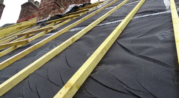 Charpente en cours d'installation, avec la membrane d'étanchéité noire prête pour l'isolation toiture. Les chevrons en bois sont posés.