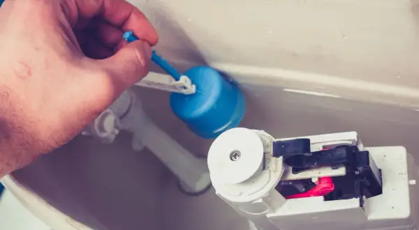Main tenant ajuste le flotteur bleu pour arrêter la chasse d'eau qui coule.
