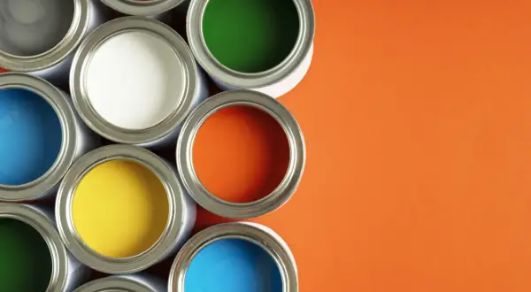 Un assortiment de pots de peinture glycero ou acrylique ouverts, révélant des couleurs vives comme le bleu, le jaune, le rouge, le vert et l'orange sur fond orange.