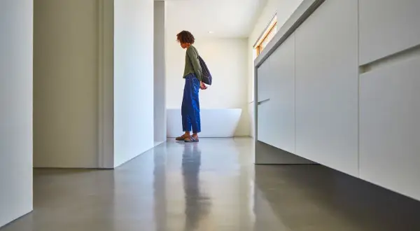 Une personne se tient sur un sol en béton ciré brillant, devant une baignoire et des meubles de salle de bain modernes.