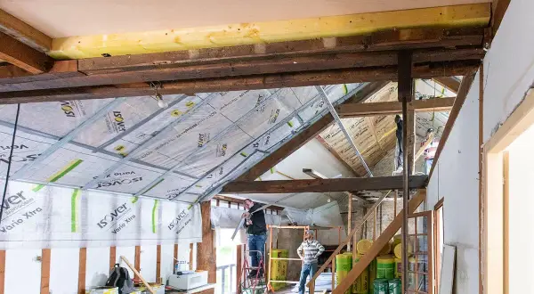 Travaux en cours pour refaire un plafond. Des ouvriers installent des rails métalliques sous les poutres apparentes.