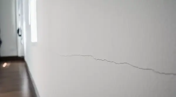 Un fin mur qui s'effrite, marqué par une longue fissure sinueuse, témoigne du passage du temps dans un couloir lumineux.
