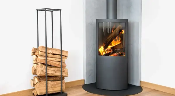 Un poêle à bois moderne avec un feu vif, à côté d'une pile de bois sur un support, le tout sur un mur en placo.