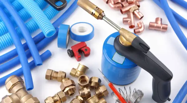 Outils pour une installation multicouche : chalumeau, tubes bleus, raccords en laiton et cuivre, coupe-tube.