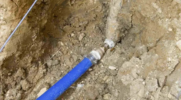 Raccordement d'une canalisation eau enterrée, respectant les normes. Le tuyau bleu est relié à une conduite plus ancienne.