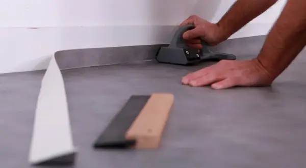 Pose lino : un artisan utilise un outil pour bien aplatir le revêtement de sol gris près du mur.