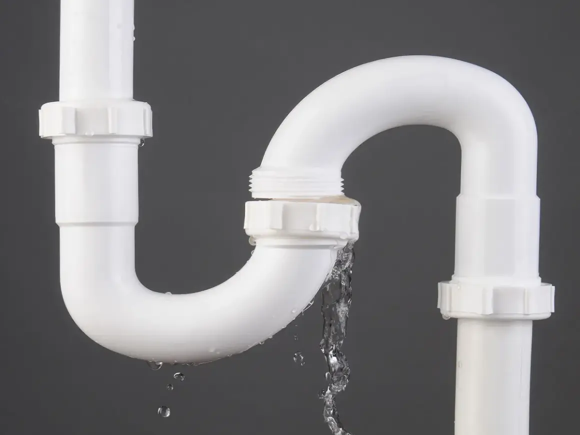 Tuyau de PVC blanc avec une fuite d'eau. Le temps de séchage de la colle PVC est crucial pour éviter ce genre de problème.
