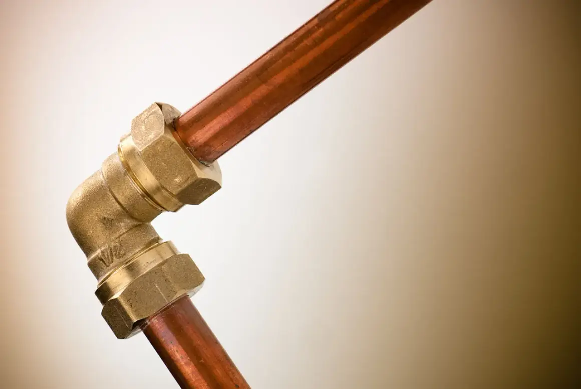 Un coude en laiton relie deux tuyaux en cuivre. Ce raccord per cuivre assure une connexion solide pour le système de plomberie.