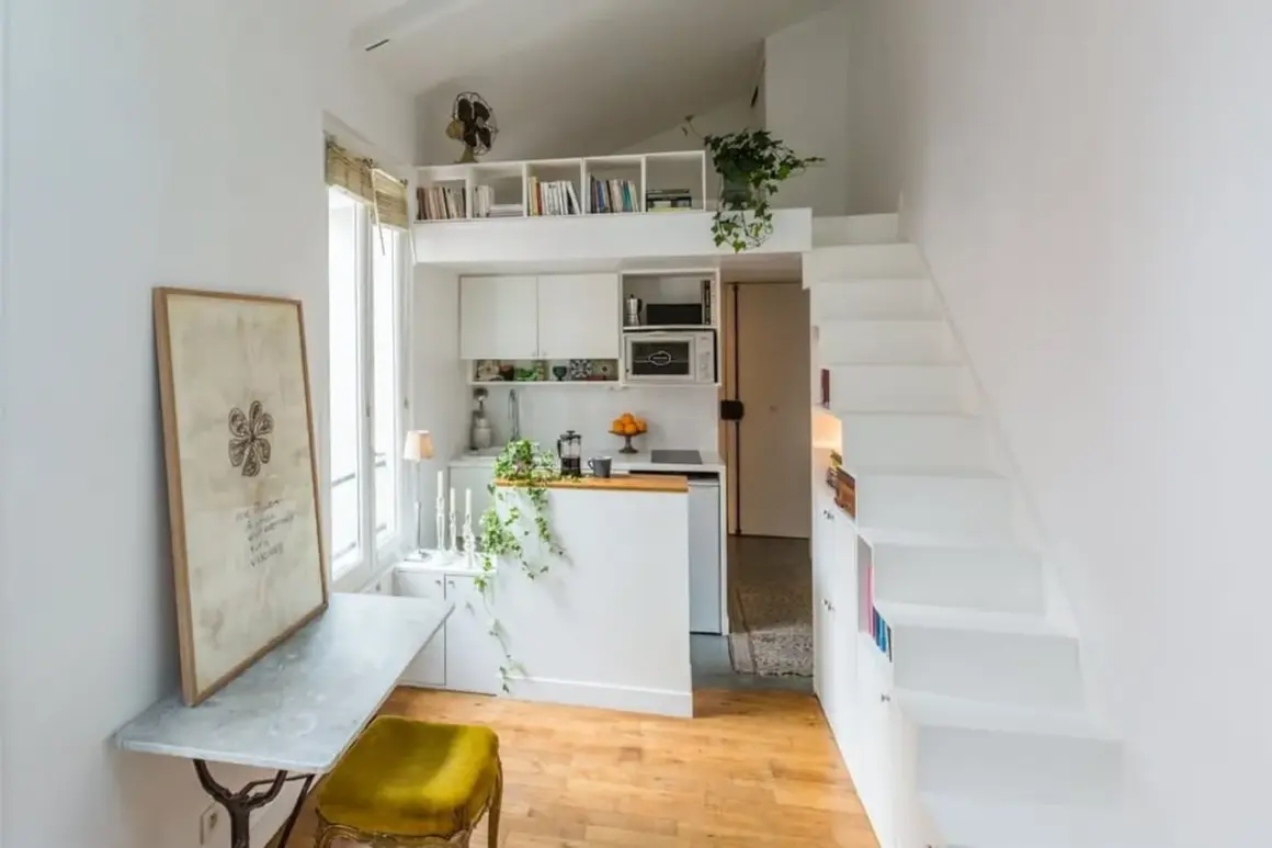Un petit appartement optimisé pour le rangement, avec une cuisine, un coin repas et des escaliers menant à une mezzanine.