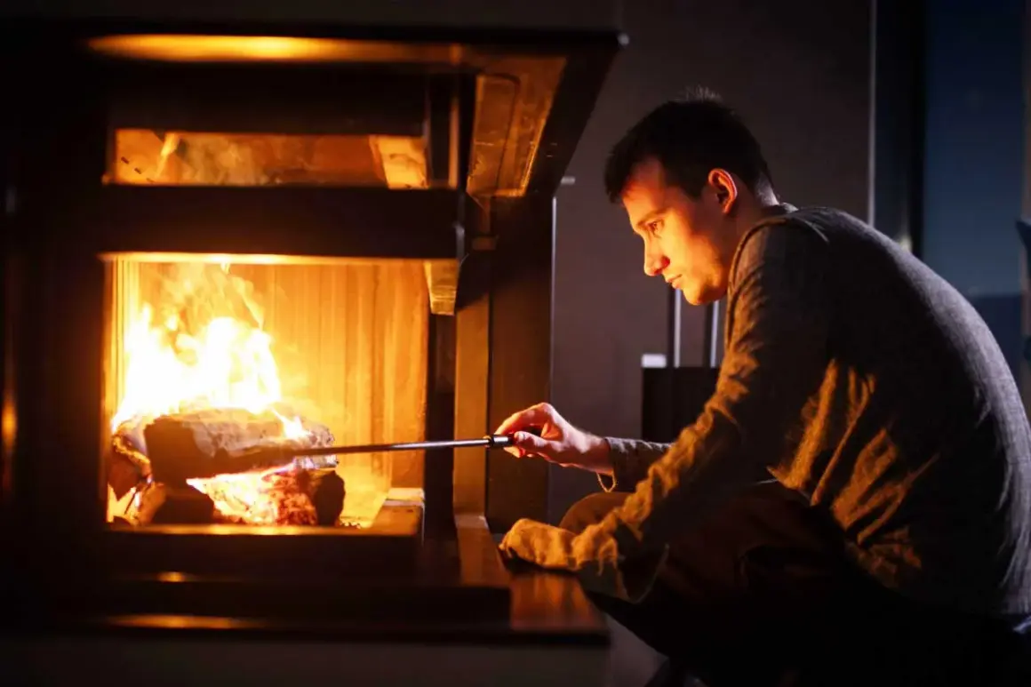 Un homme ajuste des bûches dans un poêle à bois, le feu crépite. Le tirage est parfait pour une soirée chaleureuse.